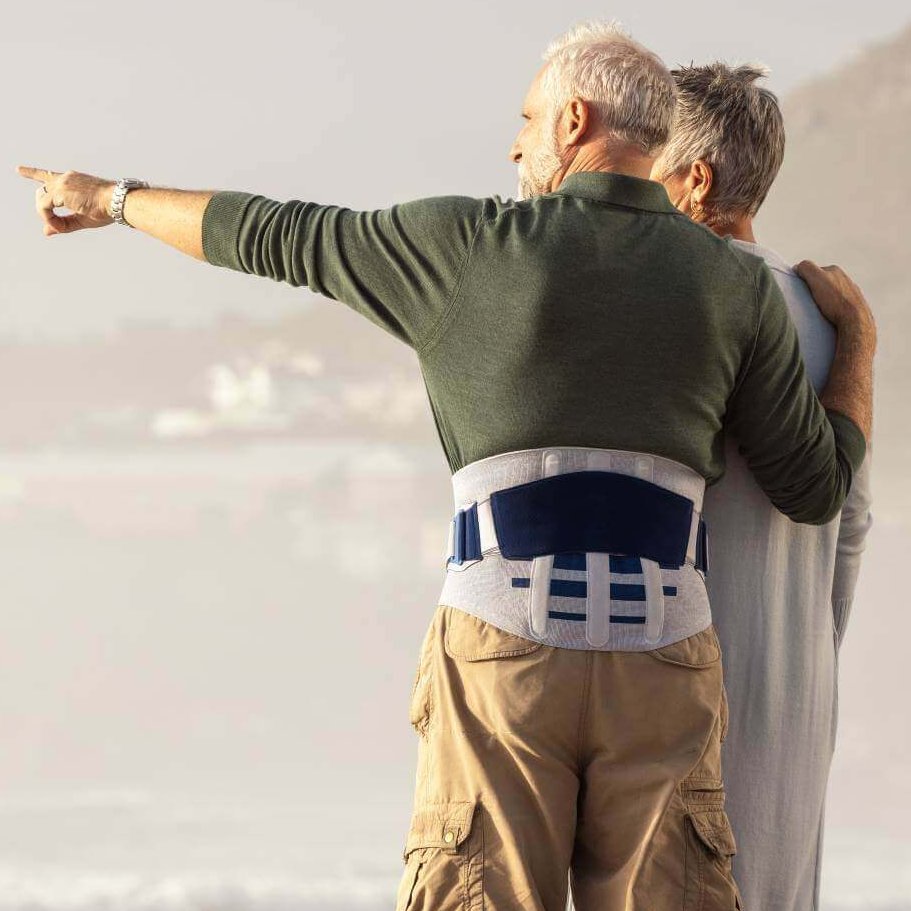 Auf dem Bild ist ein älteres Paar zu sehen. Der Mann zeigt auf etwas in der Ferne. Er trägt die LumboLoc Forte Rückenorthese von Bauerfeind.