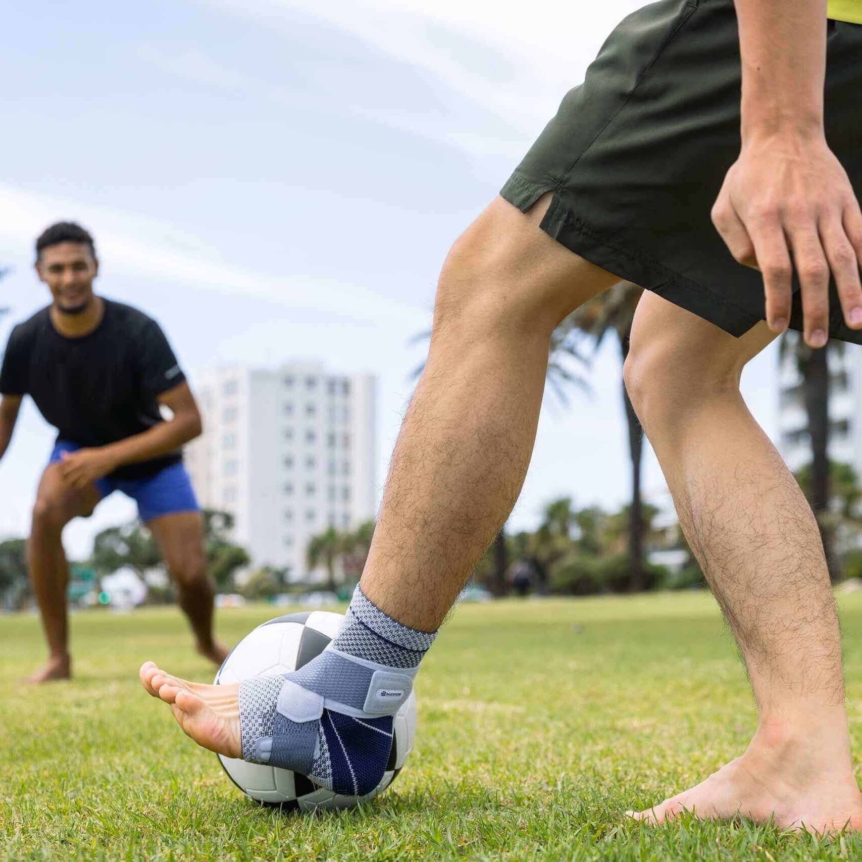 Bildausschnitt zweier Männer beim Fußballspielen im Park. Einer der Männer trägt zur Unterstützung des Sprunggelenks eine MalleoTrain Bandage am linken Bein.