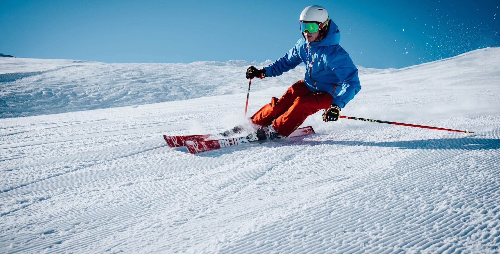 Das Bild zeigt eine Skifahrerin, die einen schneebedeckten Abhang herunterfährt. Skifahren und andere Sportarten belasten häufig das Kniegelenk.