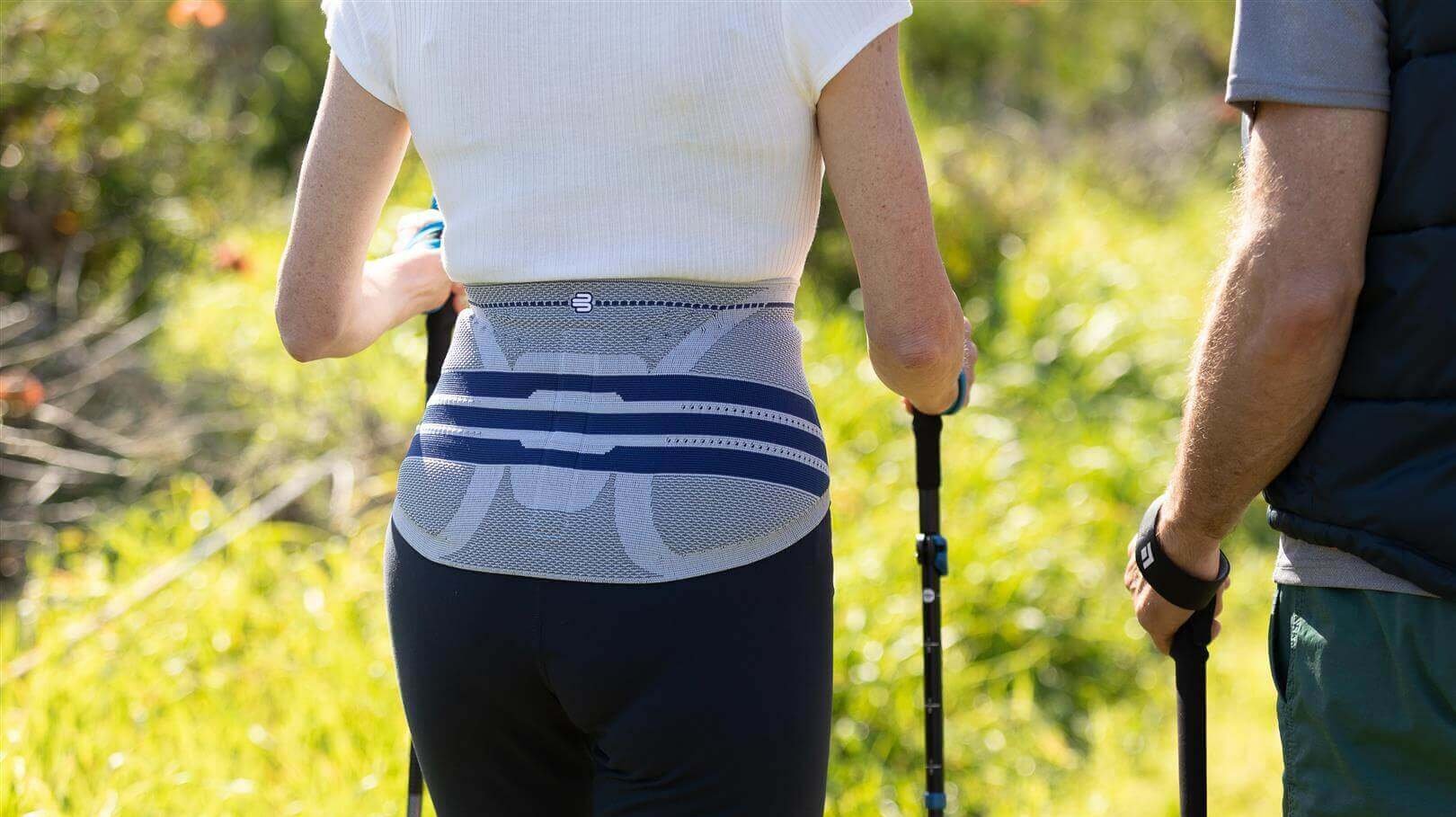 Bildausschnitt einer Frau beim Nordic Walking in der Natur, die zur Entlastung ihres Rückens eine LumboTrain Bandage trägt.