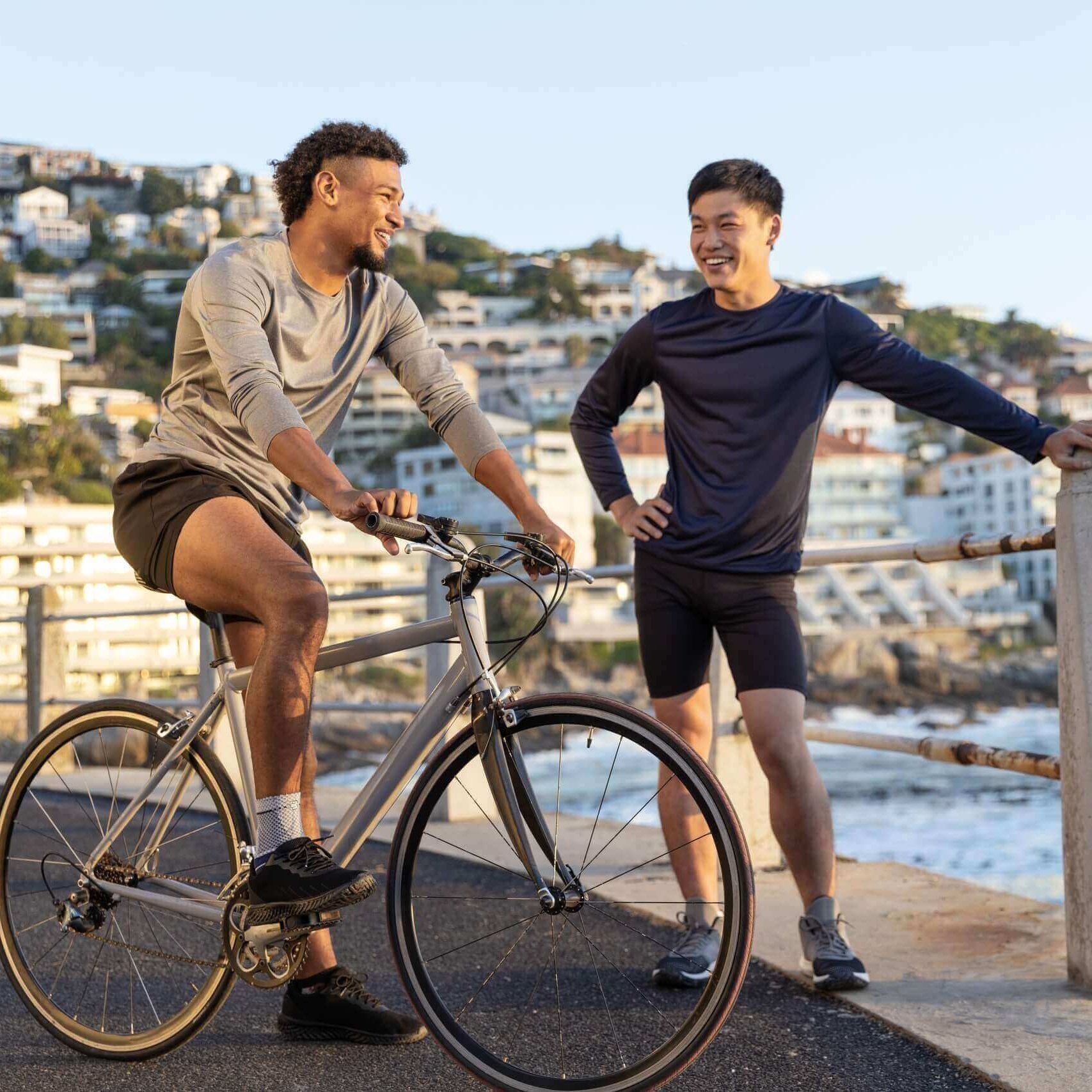 Das Bild zeigt zwei Männer an einer Strandprommenade. Einer von ihnen sitzt auf einem Fahrrad und trägt eine MalleoTrain Bandage zur Unterstützung am Fußgelenk.