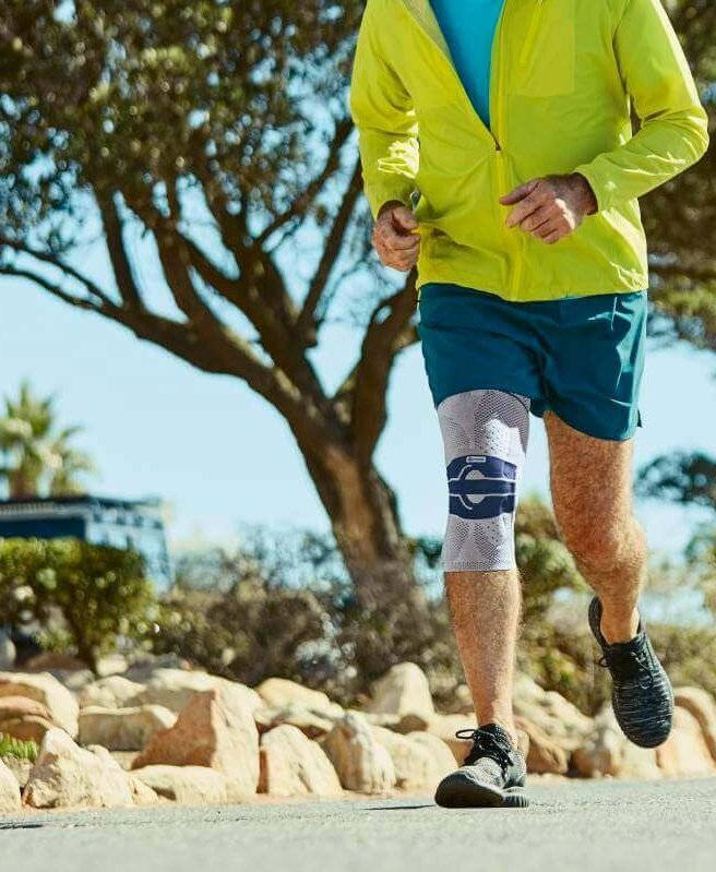 Das Bild zeigt einen älteren Mann, der im Park joggt. Um sein Knie zu unterstützen, trägt er eine GenuTrain A3 Kniebandage, die speziell für Menschen mit Arthrose entwickelt wurde.
