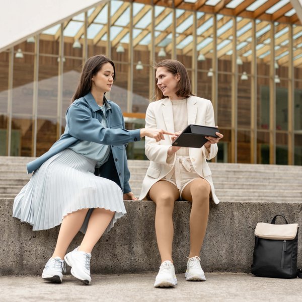 Auf dem Bild sitzen zwei Frauen auf einer Steinmauer. Sie unterhalten sich. Beide tragen VenoTrain micro Kompressionsstrümpfe von Bauerfeind.