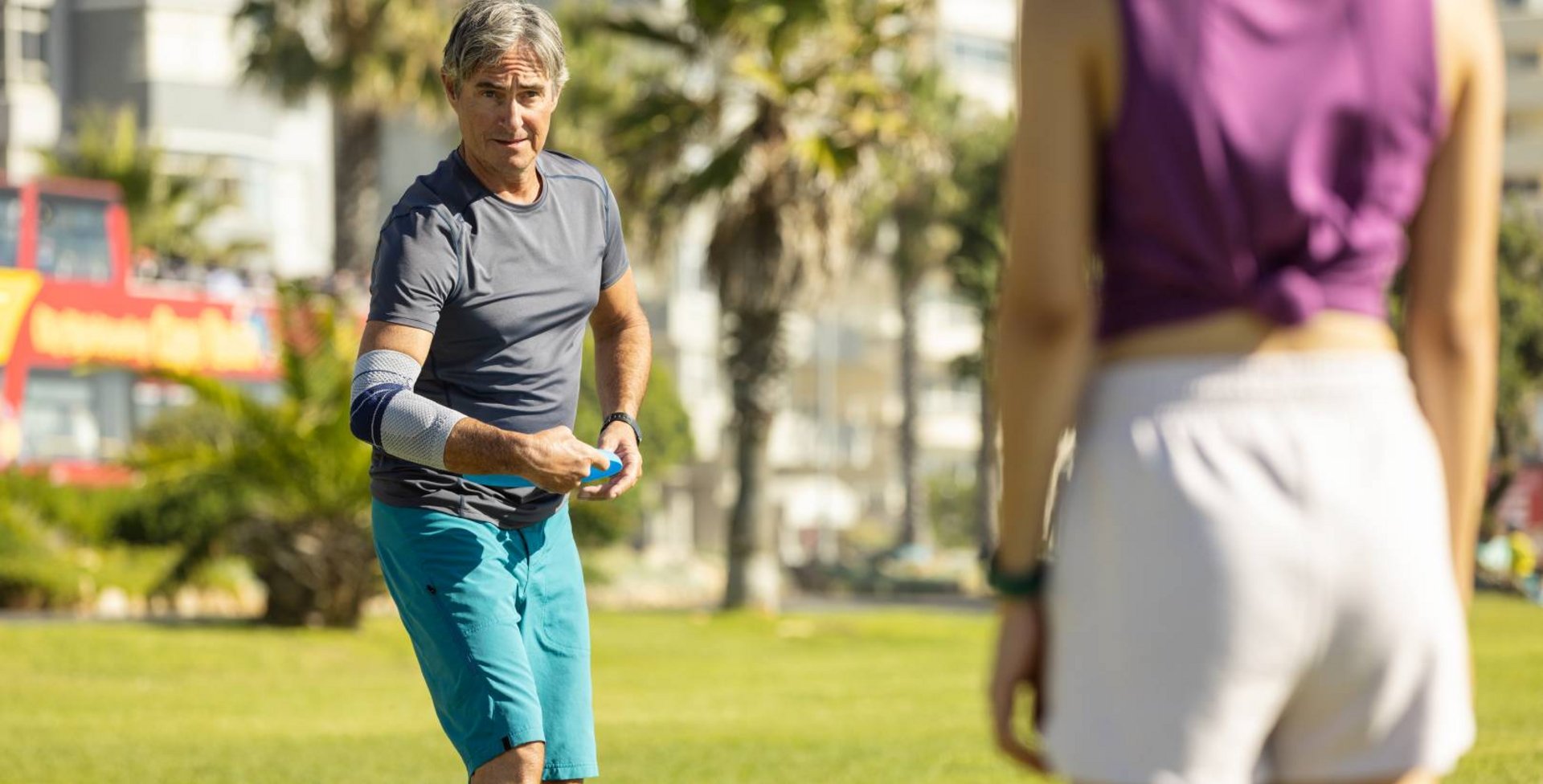 Dieses Bild zeigt eine Frau und einen Mann mit EpiTrain Ellenbogenbandagebei Frisbee-Spielen im Park. Um Beschwerden im Ellenbogen vorzubeugen, trägt der Mann eine EpiTrain Bandage von Bauerfeind.