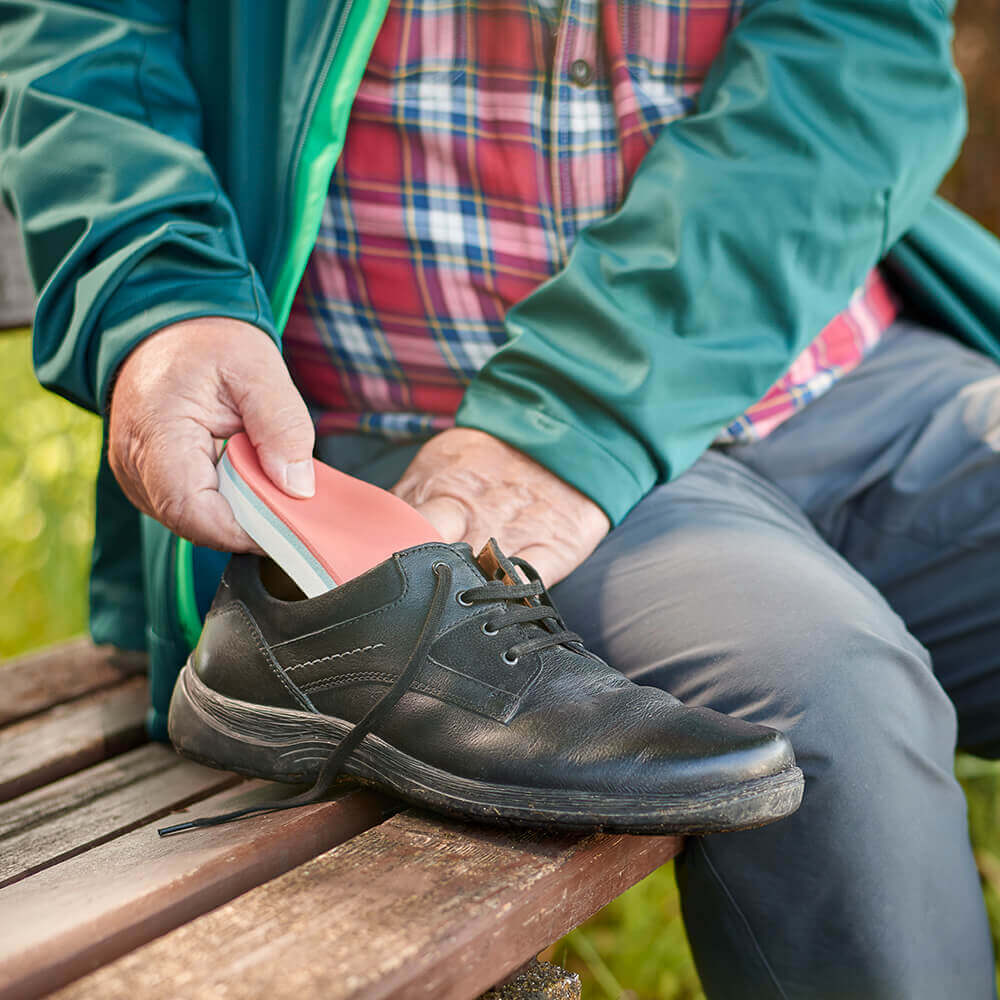Ein Mann sitzt auf einer Bank und legt eine ErgoPad soft Diabetes Schuheinlage von Bauerfeind in seinen Schuh ein. Hochwertige Weichpolster-Einlagen wie die ErgoPad soft Diabetes von Bauerfeind helfen Diabetikern dabei, Druckstellen und Wunden an den Füßen während des Laufens zu vermeiden.