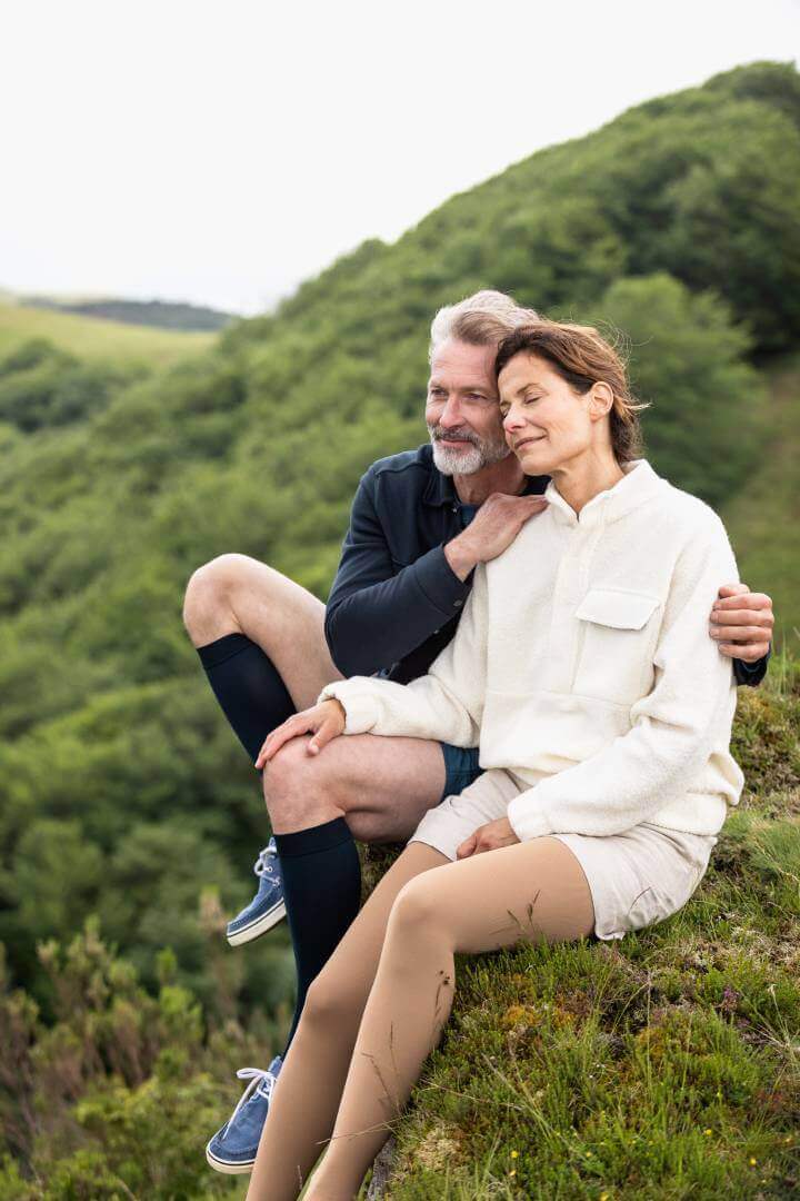 Zwei Personen sitzen auf einem Felsen der mit Moos bewachsen ist. Sie tragen beide VenoTrain Impuls Kompressionsstrümpfe von Bauerfeind.