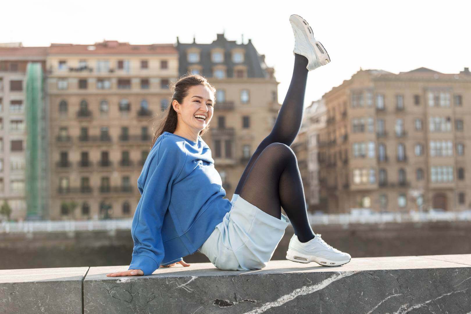 Eine Frau, die auf einer Steinmauer sitzt. Sie streckt dabei ein Bein nach oben. Sie trägt Kompressionsstrümpfe von Bauerfeind.